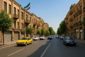 نمایی از خیابان لاله‌زار نو تهران در روزی آفتابی، با ساختمان‌های آجری تاریخی، درختان سبز در دو طرف خیابان، خودروها و تاکسی زرد در حال حرکت و پرچم ایران برافراشته بر بالای یکی از ساختمان‌ها.