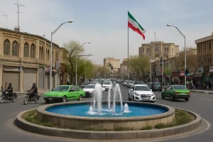 نمایی واقعی از میدان قیام در یکی از شهرهای ایران، با حوض و فواره‌ای آبی در مرکز میدان، خودروها و موتورسیکلت‌های در حال عبور، ساختمان‌های آجری تاریخی و پرچم ایران که در پس‌زمینه در اهتزاز است.