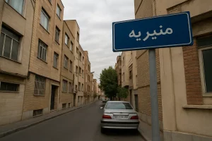 تابلوی آبی‌رنگی با نوشتهٔ «منیریه» در ابتدای کوچه‌ای باریک دیده می‌شود؛ دو طرف خیابان ساختمان‌های آجری و کرم‌رنگ قرار دارند و یک خودروی نقره‌ای در کنار پیاده‌رو پارک شده است.