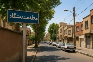 نمایی از محله صد دستگاه در تهران، خیابانی آرام با ساختمانهای آجری، درختان سایهدار و خودروهای پارکشده در دو طرف خیابان در یک روز آفتابی.