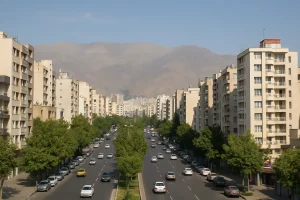 «نمایی از خیابان عریض و پررفتوآمد در شمالشرق تهران، با ساختمانهای بلند مسکونی در دو طرف و کوههای البرز در پسزمینه، در یک روز صاف و آفتابی.»