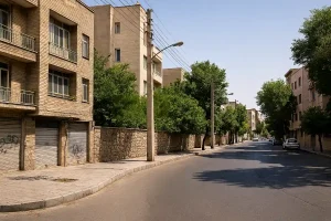 «نمایی از یک خیابان آرام و خلوت در محلهای شهری با ساختمانهای آجری، درختان سرسبز دو طرف خیابان و نور روز تابستانی.»