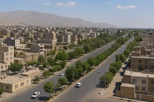 «نمایی هوایی از محلهای شهری در تهران با ساختمانهای کمارتفاع، خیابان عریض دوطرفه پوشیده از درخت، چند خودرو در حال حرکت و کوههای کمارتفاع در پسزمینه در یک روز آفتابی.»